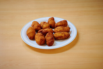 A plate of fried chicken pieces sits on a wooden table. The chicken pieces are golden brown and appear to be seasoned well