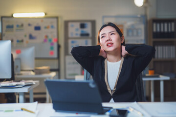 Young manager having pain in her neck while working on a laptop in office at night, concept of work related stress and health problems