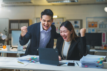 Two joyful Asian businesspeople celebrating their success together in a modern office, working...