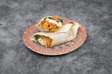 A burrito is on a plate. The plate is red and white. The burrito is wrapped in a tortilla