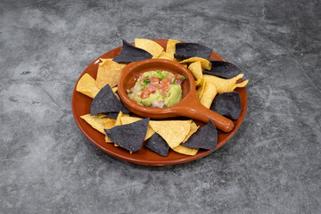 A plate of tortilla chips with a bowl of guacamole. The bowl is in the center of the plate and the chips are scattered around it