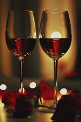 Romantic evening with two glasses of red wine surrounded by rose petals and soft candlelight