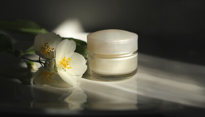 White jasmine flowers with jar of cosmetic cream. Natural cosmetics for facial skin care.