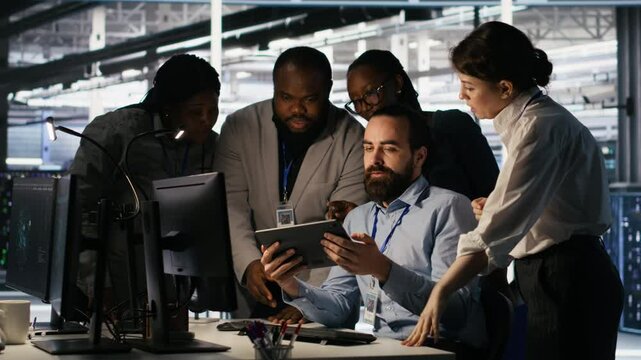 Data center system administrators performing maintenance on supercomputers used for AI processing. Team managing server hub rigs used for deep learning training, looking over business charts, camera A