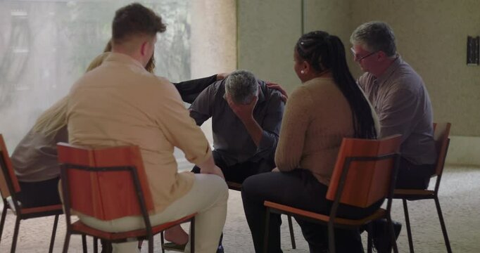 Man opens up emotionally during group therapy session, leaning forward while expressing vulnerability and receiving support from compassionate peers seated in circle