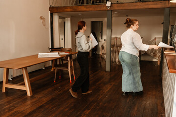 A woman owner and a woman employee hold papers while they go to a bar, a cafe
