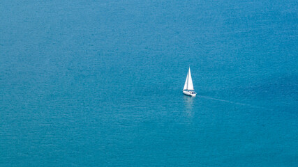 Aerial view of a white and lonely sailboat in the middle of the blue sea.