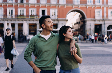 Interracial couple exploring historic square arm in arm, looking around with awe and admiration, experiencing travel magic in romantic European setting full of charm and energy © BullRun