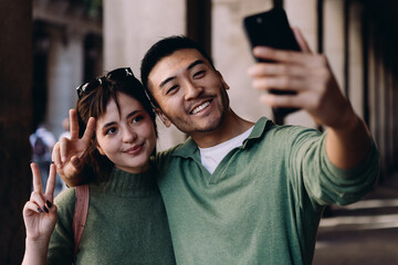 Happy couple taking selfie, flashing peace signs while smiling. Playful mood, urban setting, and youth culture blend in an expressive and candid moment