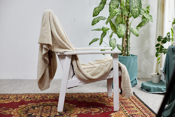 Cozy chair draped with a blanket in a calming interior setting with plants and a patterned rug