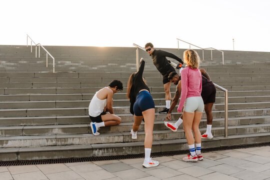 A group of five athletes are warming up and stretching while standing on the stairs outdoors