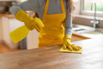 Cleaning in a bright kitchen with yellow gloves and spray bottle while wiping the counter surface on a sunny day © Iryna