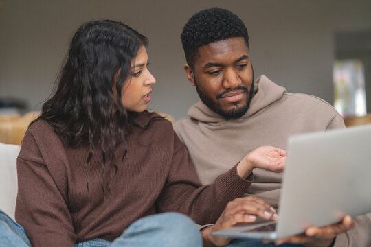 Two people engaged in discussion while working on a laptop in a cozy living room setting during a sunny afternoon