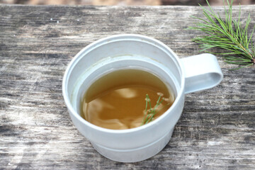 tea in a mug on a wooden table, a pine branch lies nearby