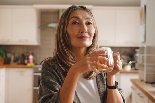 Middle-aged woman enjoys her beverage in a cozy kitchen while contemplating her day in the late afternoon light