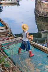 Little fisherman boy wearing straw hat on wooden boat near harbor
