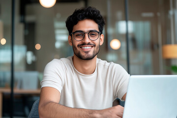 Young Indian student sitting at desk using laptop smiling and looking at camera