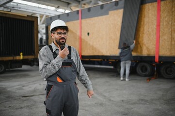 Arab engineer using walkie talkie supervising modular house production in construction workshop