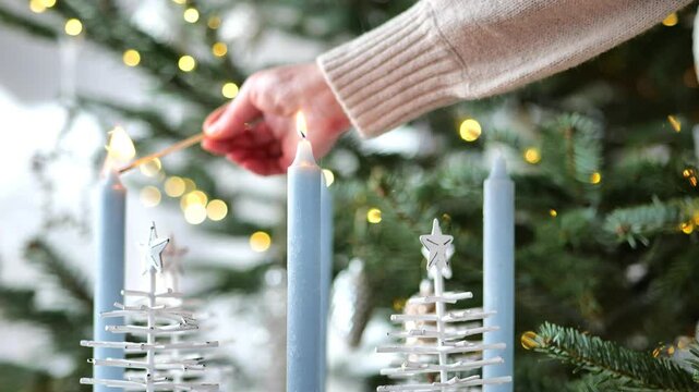 Christmas wreath with candles.Second Advent. Hand lights blue candle in Advent wreath on Christmas tree background. The second week before Christmas.Winter holidays atmosphere.