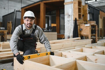 Carpenter checking level of wooden frame for prefabricated modular house