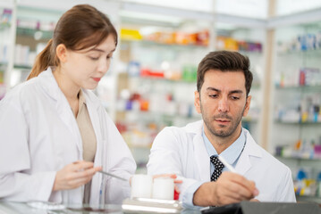 Two pharmacists counting drug pills arranging assortment working in drug shelves counter