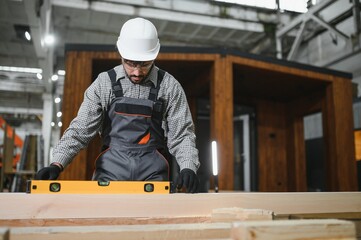 Construction worker using spirit level on wooden beam in workshop