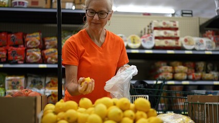 Slow motion view of smiling happy pretty mature woman selecting lemons in a grocery store.