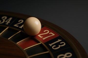 Close up of roulette ball landing on the number twenty seven on a wooden roulette wheel, suggesting casino gambling and games of chance