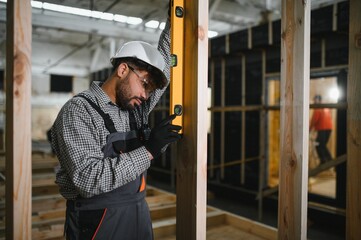 Construction worker checking verticality of wooden beam with spirit level in modular house...