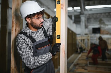 Construction worker using spirit level on wooden beam in workshop