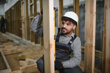 Construction worker checking verticality of wooden beam with spirit level in modular house...