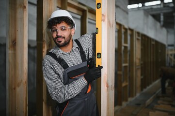 Construction worker using spirit level on wooden beam in workshop