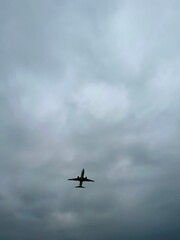 Vertical photo of airplane silhouette against dramatic gray sky, moody atmosphere, aviation theme, travel concept, stormy weather, flying aircraft, minimal scene, cloudy sky, air transport. 