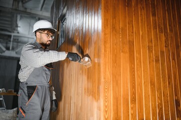 Construction worker applying varnish on wooden wall of modular house