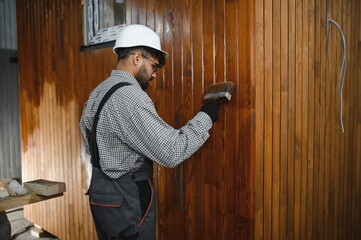 Construction worker applying varnish on wooden panels of prefabricated house