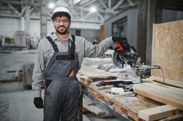 Arab carpenter operating compound miter saw in workshop for modular house production