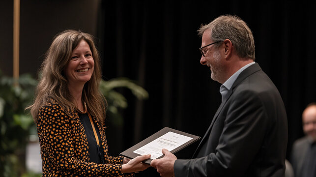 A woman happily receives a document from a man during a formal ceremony, smiling brightly.