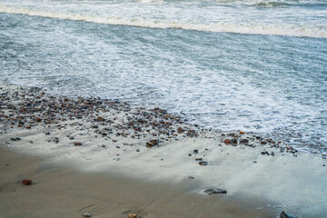 Waves softly roll onto a sandy beach scattered with smooth pebbles capturing the early morning light The shoreline creates a serene atmosphere perfect for reflection