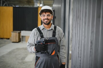 Construction worker holding cordless drill assembling modular house in workshop