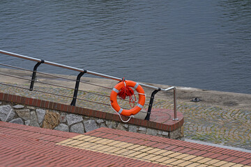 Orange lifebuoy hanging on the banisters of the stairs on the river embankment