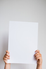 Child holding blank white paper against neutral background