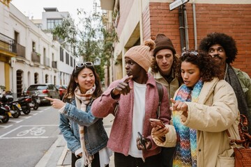 A group of five friends stand while three of them point to the sides, on the street