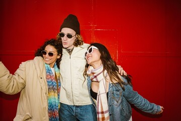 Group of three friends standing and hugging while smiling and posing, on a red background