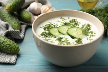 Tasty cucumber soup in bowl and ingredients on light blue wooden table, closeup