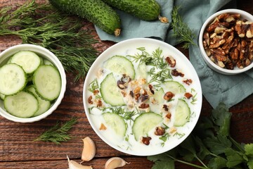 Tasty cucumber soup with dill, nuts and garlic on wooden table, flat lay
