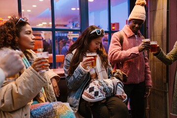 A group of five friends hold glasses while two of them clink glasses, outdoors