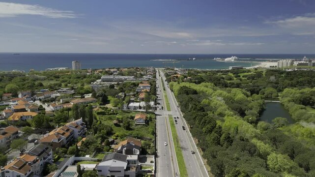Drone flies northwest along Avenida da Boavista next to Parque da Cidade do Porto on sunny day in Porto, Portugal