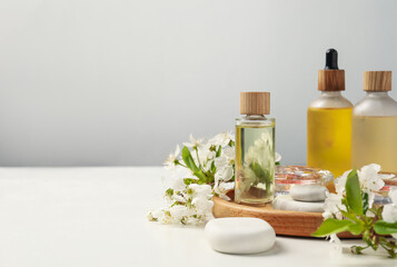 Spa products, pebble stones and twigs with beautiful flowers on white table against grey background, closeup. Space for text