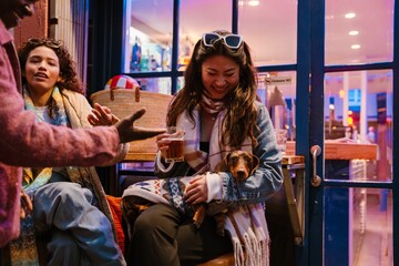 Group of three friends talking and smiling while one of them holds a dog and a glass, outdoors