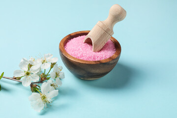 Sea salt in bowl, scoop and twigs with beautiful flowers on light blue background
